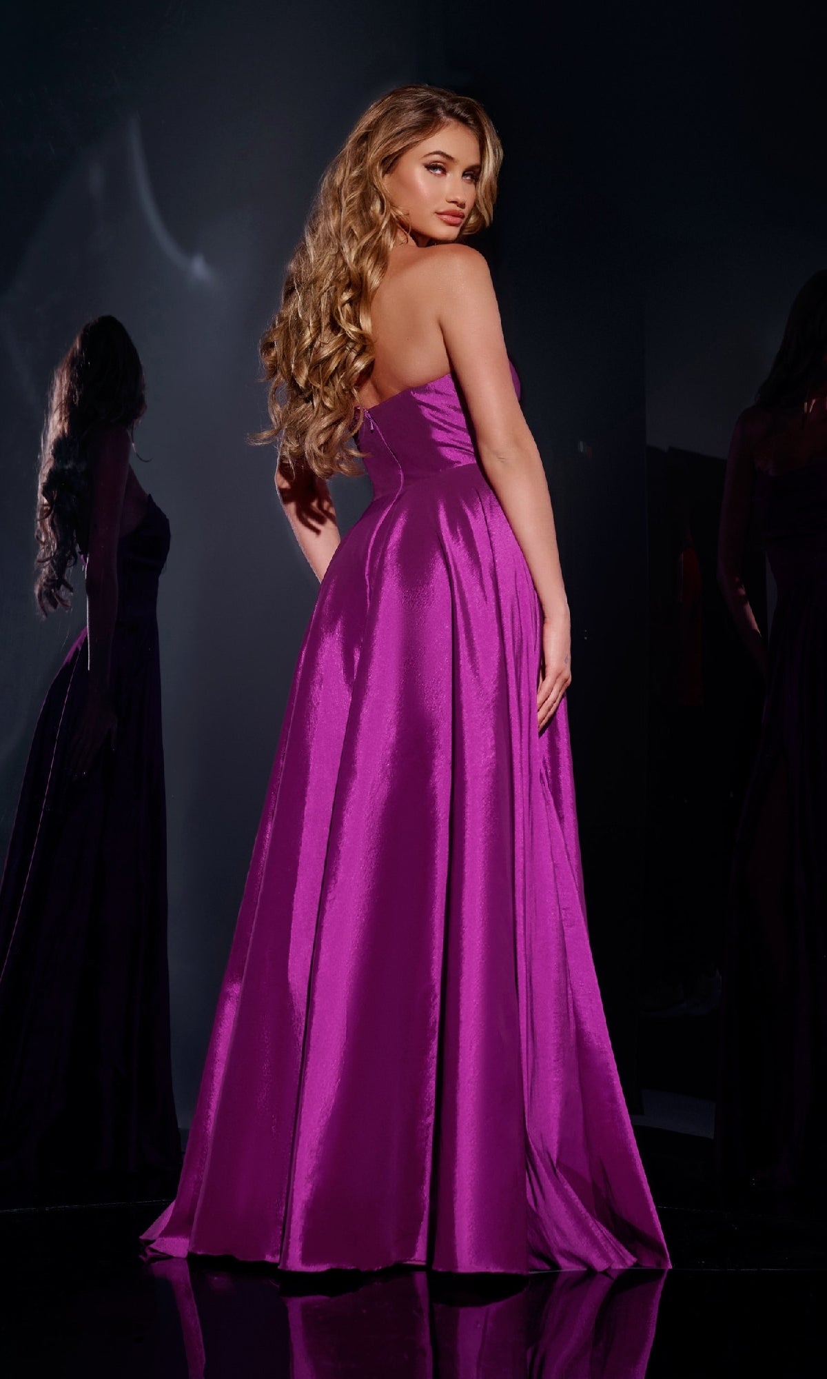 A woman with long wavy hair wears the Jovani D5822 long prom dress in vibrant purple, standing with her back turned and looking over her shoulder.